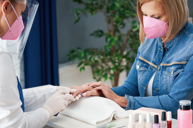 senhora sênior usando máscara em salão de manicure