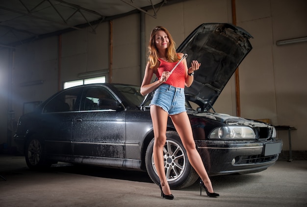Senhora sexy em pé perto de carro na oficina de reparação automóvel