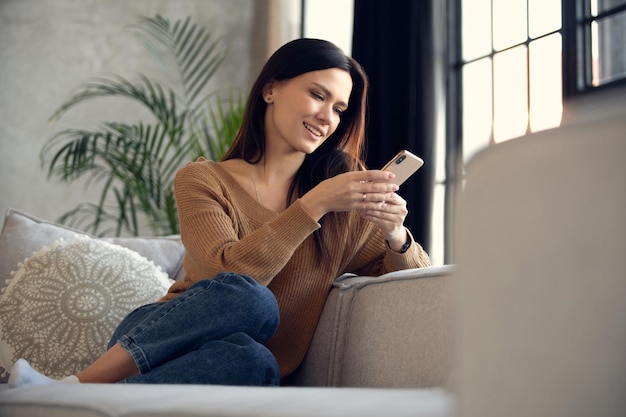 Senhora sorridente de 30 anos conversando em redes sociais assistindo a vídeos engraçados usando aplicativos móveis em casa