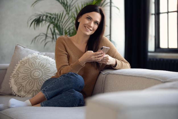 Senhora sorridente de 30 anos conversando em redes sociais assistindo a vídeos engraçados usando aplicativos móveis em casa