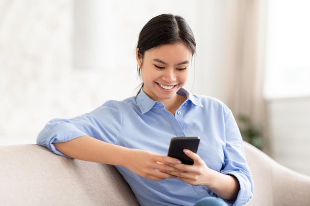 Senhora sorridente sentada no sofá usando o espaço de cópia do telefone celular