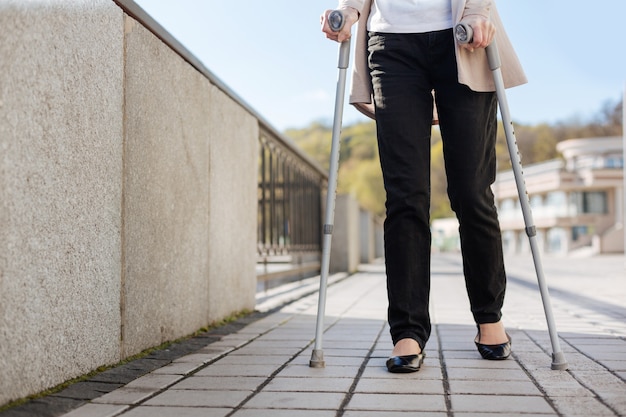 Senhora tímida e moderna segurando muletas nas mãos e dando passos enquanto caminhava pelo cais