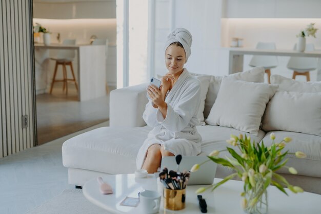 senhora toca o rosto suavemente aplica creme facial durante uma videochamada com o smartphone