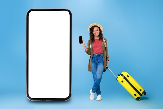 Senhora viajante negra mostrando smartphone em pé perto do fundo azul do celular