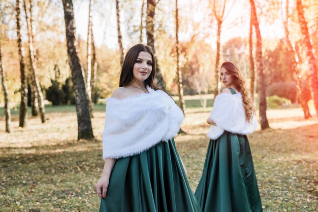 Senhoras em elegantes vestidos verdes, caminhando no parque outono. menina morena garotas sonhadoras rindo ao ar livre