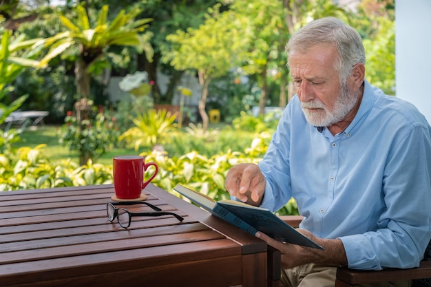 Senior anciano leyendo libro con taza de café en el jardín