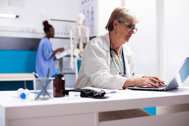 Senior-Arzt schreibt am Schreibtisch auf dem Laptop