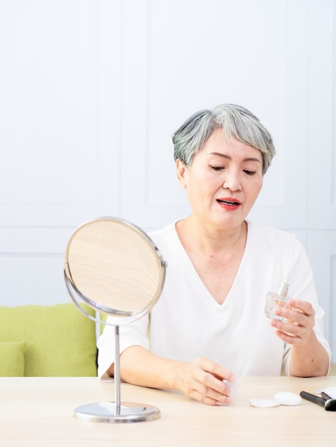 Senior Asia Woman sprüht Parfüm zu Hause.