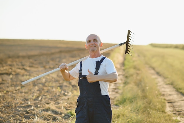 Foto senior bauer steht auf einem feld mit einem rechen