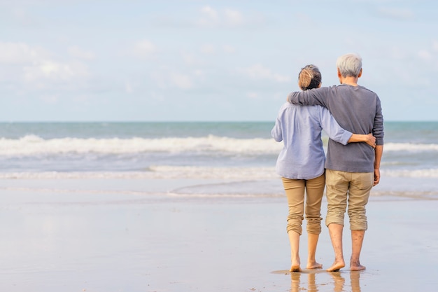 Senior casal asiático andando na praia de mãos dadas. Família de lua de mel juntos estilo de vida felicidade. Vida após a aposentadoria. Plano de seguro de vida