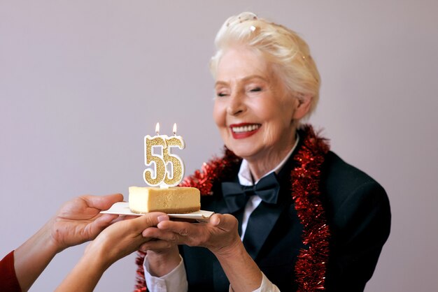 sênior elegante de smoking soprando uma vela cinquenta e cinco em seu bolo de aniversário