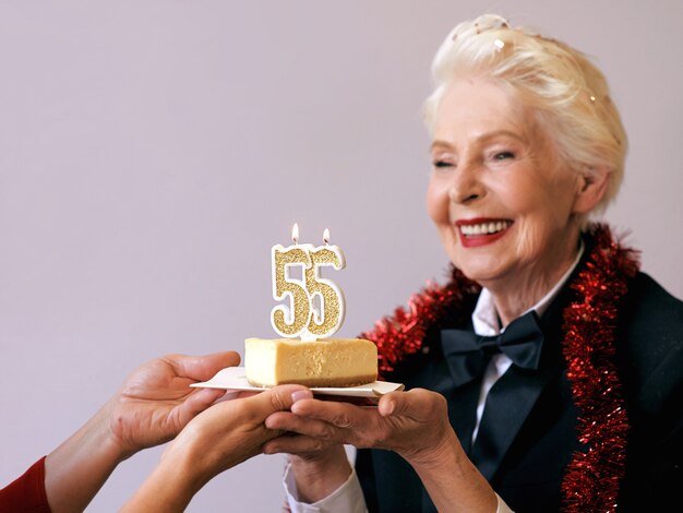 Senior elegante mujer en esmoquin soplando velas cincuenta y cinco en su tarta de cumpleaños