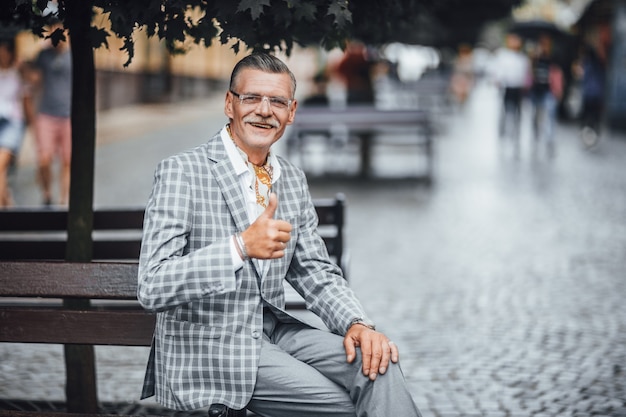 Senior empresario barbudo mostrando bien emplazamiento en la calle