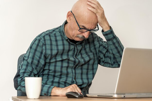 Senior empresario delante de la computadora portátil con dolor de cabeza