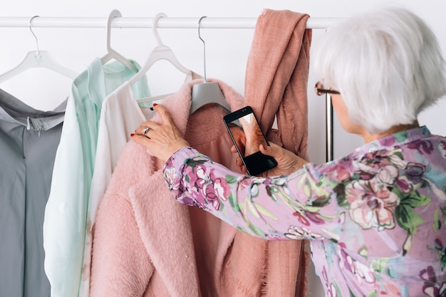 Senior Fashion-Stylist bei der Arbeit. Erfolgreiche Geschäftsfrau. Ältere Frau, die mobiles Foto macht. Personalisierter Einkaufsservice.