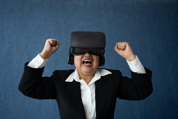 Senior-Geschäftsfrau trägt intelligente virtuelle Brille für Videokonferenzen VR-Headset-Brille-Technologie in modernen Büros und hebt Ihre Arme, um Erfolg zu zeigen Metaverse-Konzept