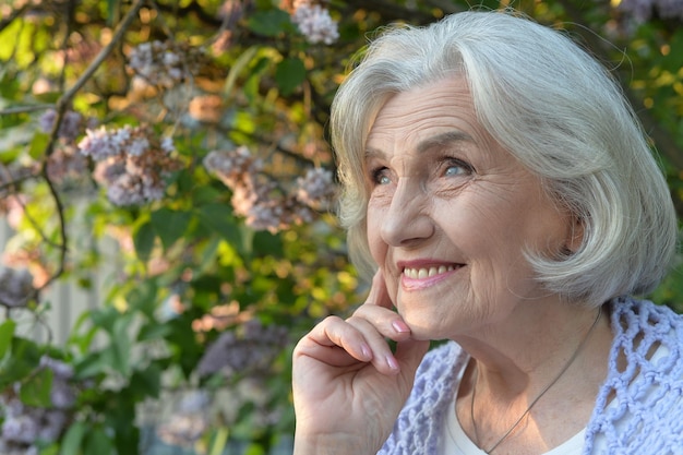Senior hermosa mujer feliz posando por lilas en el parque