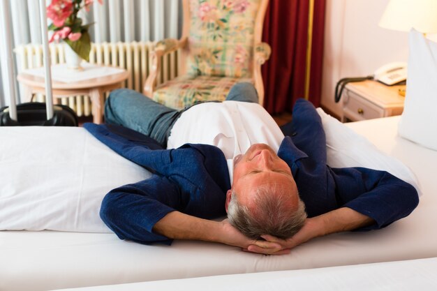 Senior hombre acostado en la cama en la habitación del hotel