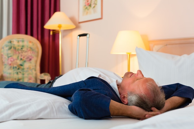 Senior hombre acostado en la cama en la habitación del hotel