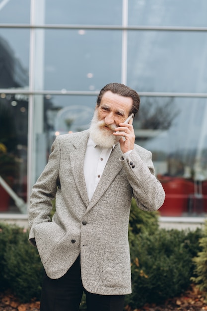 Senior hombre con barba gris y bigote en una chaqueta habla por teléfono
