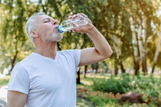 Senior hombre bebiendo agua después de hacer ejercicio en el parque