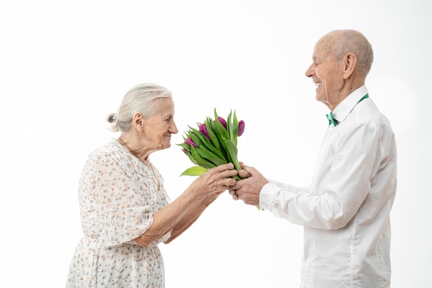 Senior hombre de camisa blanca da flores a anciana