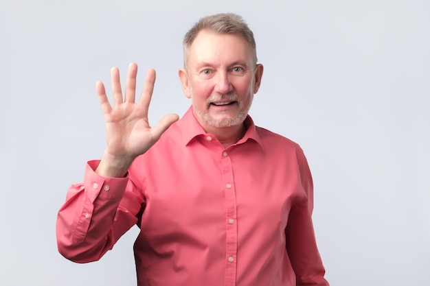 Senior hombre en camisa roja ola mano bienvenida