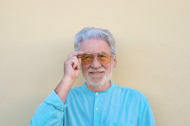 Senior hombre canoso y barbudo sobre fondo amarillo tocando gafas de sol