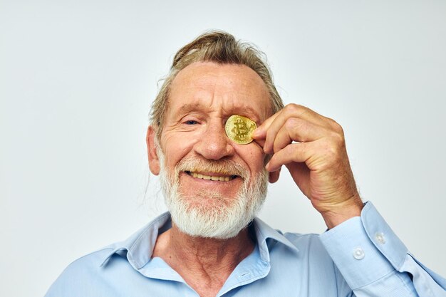 Senior hombre canoso financia monedas de oro bitcoin cerca de la cara de fondo claro