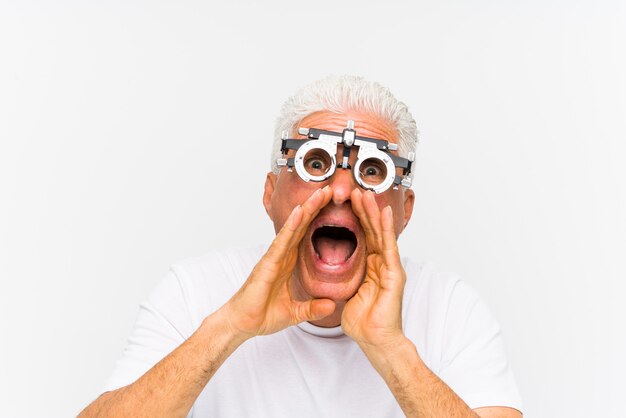 Senior hombre caucásico vistiendo un marco de prueba optometrista gritando emocionado al frente.