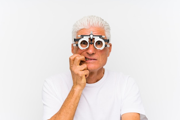 Senior hombre caucásico vistiendo un marco de prueba optometrista morderse las uñas, nervioso y muy ansioso.