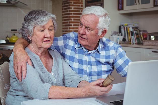 Senior hombre consoladora esposa sosteniendo contenedor de píldoras