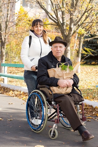 Senior hombre discapacitado yendo de compras ayudado por una atractiva mujer sonriente