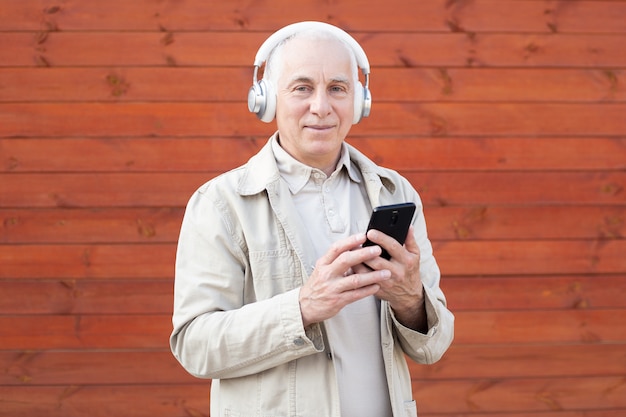 Senior hombre divirtiéndose con smartphone móvil y con auriculares. Concepto de felicidad, tecnología y estilo de vida de personas mayores