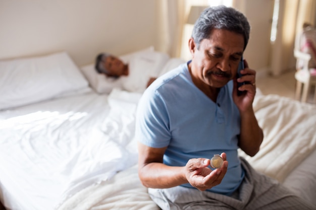 Senior hombre hablando por teléfono móvil mientras mira la medicina en el dormitorio