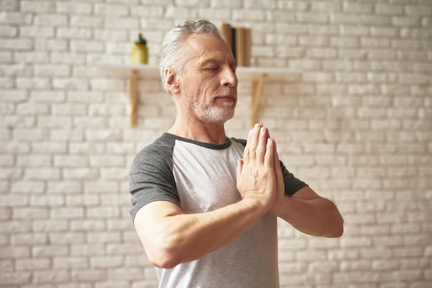 Senior hombre hace ejercicios de yoga con los ojos cerrados.