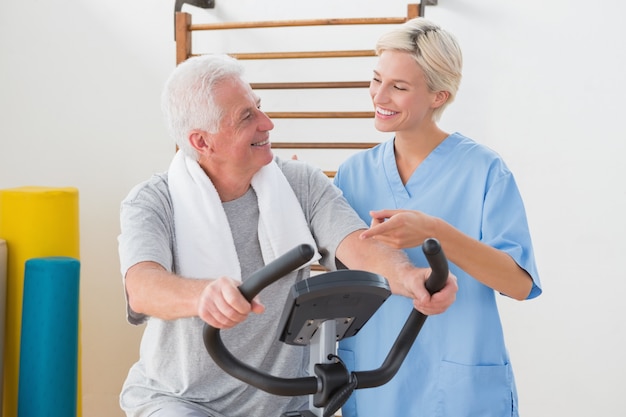 Senior hombre haciendo bicicleta estática con terapeuta