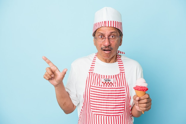 Senior hombre helado americano sosteniendo un helado aislado sobre fondo azul apuntando hacia el lado