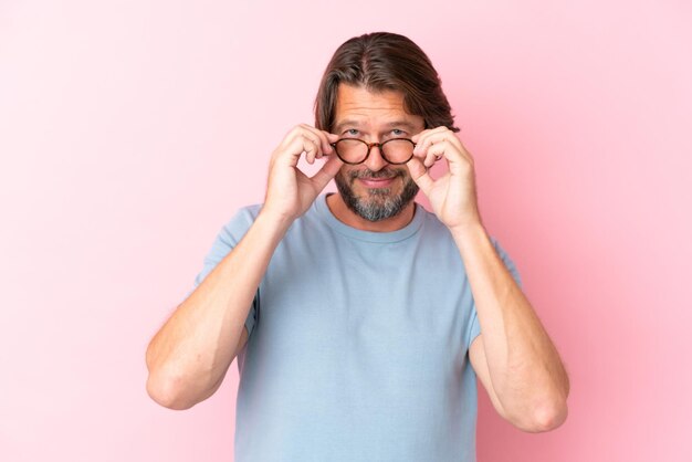 Senior hombre holandés aislado sobre fondo de color rosa con gafas con expresión feliz