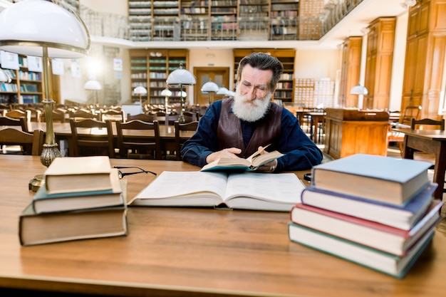 Senior hombre lector se sienta en el interior de la biblioteca antigua de lujo y lee el libro. Hombre barbudo con cara feliz disfruta leyendo.