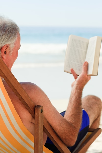 Senior hombre leyendo un libro en la playa