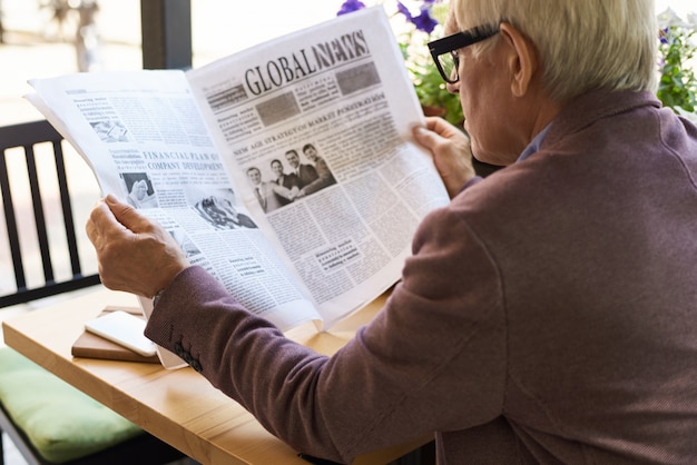 Senior hombre leyendo periódico en el desayuno