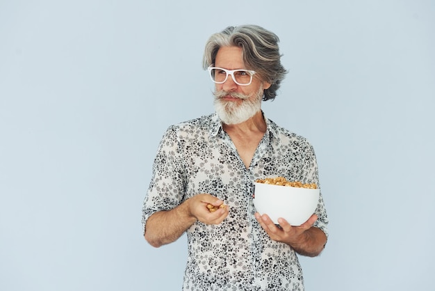 Senior hombre moderno con estilo con pelo gris y barba en el interior con palomitas de maíz