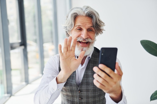 Senior hombre moderno con estilo con pelo gris y barba en el interior