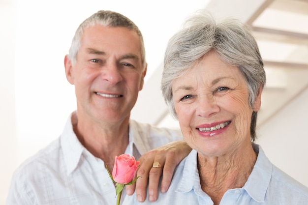 Senior hombre ofreciendo una rosa a su compañero sonriendo a la cámara