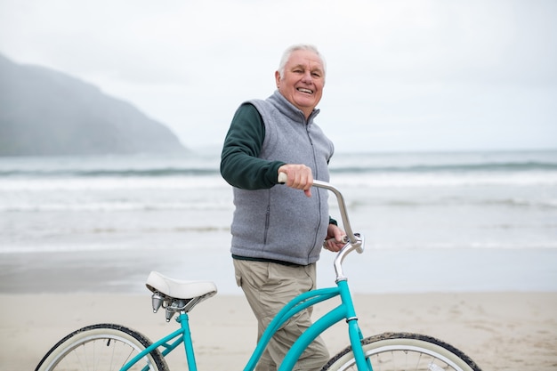 Senior hombre parado con bicicleta en la playa