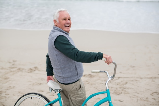 Senior hombre parado con bicicleta en la playa