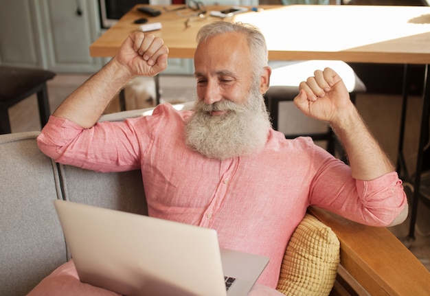 Senior hombre sentado en un sofá frente a una computadora portátil