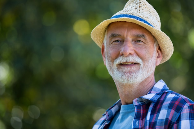 Senior hombre con sombrero de pie en el jardín