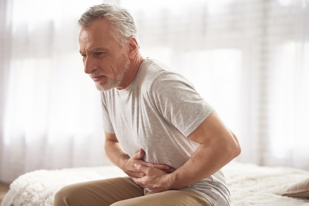 Senior hombre tiene dolor de estómago en la cama en la mañana.